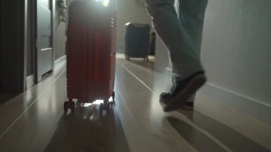Dolaşan bavullarla kapıya doğru yürüyen bir gezginin arka görüntüsü. Koridorda turuncu bavulla yürüyen kişi. Ayrılma ve tatil için evden ayrılma kavramı