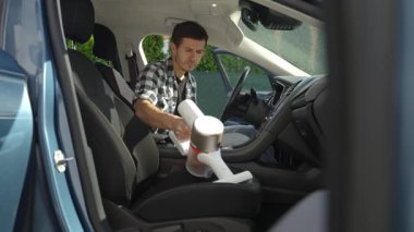 Adam araçta koltuk döşemesini temizlemek için el yapımı elektrikli süpürge kullanıyor. Modern araba temizliği ve bakımı