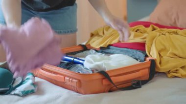 Kadın renkli kıyafetleri yatak odasında turuncu bavula katlıyor. Tatil hazırlığı, seyahat gereksinimleri ve paketleme süreci kavramı