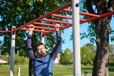 Erkek sporcu, spor salonunda kırmızı maymun parmaklıklarında antrenman yapıyor. Adam sağlık ve vücut kontrolü için açık hava parkında spor egzersizleri yapıyor. Zindelik, dayanıklılık ve sağlıklı yaşam tarzı kavramı