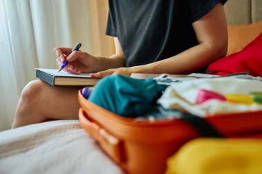 Deftere, içi kıyafet dolu turuncu bir bavul yazmış. El yazısıyla kontrol listesi olan seyahat kavramı