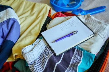 El yazısıyla kontrol listesi ve bavula doldurulmuş kıyafetlerin üzerindeki kalem. Yolculuğa hazırlanıyorum. Tatil ve tatil planlama