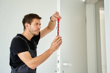 İşçi, balon seviyesiyle kapının dikey hizasını kontrol ediyor. Profesyonel iç kapı döşemesi. Ev yenilenmesi