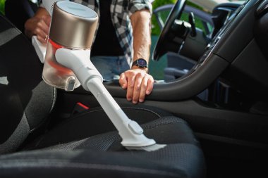 Adam araçta koltuk döşemesini temizlemek için el yapımı elektrikli süpürge kullanıyor. Modern araba temizliği ve bakımı