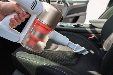 Adam araçta koltuk döşemesini temizlemek için el yapımı elektrikli süpürge kullanıyor. Modern araba temizliği ve bakımı