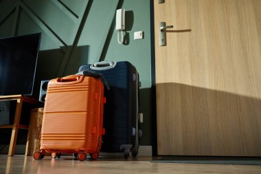 İki modern bavul, turuncu ve lacivert, sabah ışığında giriş kapısının yanında durun. Oturma odasındaki bavullar tatil için hazır. Seyahat hazırlığı kavramı