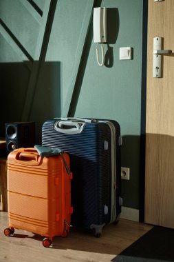 İki modern bavul, turuncu ve lacivert, sabah ışığında giriş kapısının yanında durun. Oturma odasındaki bavullar tatil için hazır. Seyahat hazırlığı kavramı