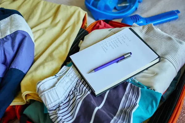 El yazısıyla kontrol listesi ve bavula doldurulmuş kıyafetlerin üzerindeki kalem. Yolculuğa hazırlanıyorum. Tatil ve tatil planlama