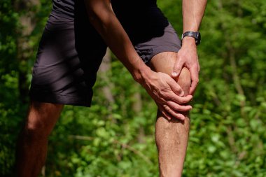 Yaz parkında antrenman yaparken dizinde ağrı olan bir koşucu. Adam koşarken yaralanmış. Spor sonrası diz ağrısı çeken erkek sporcu.