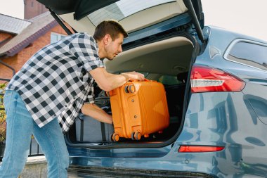 Yolculuğa hazırlanan adam, bavulu bagaja yüklüyor. Yolculuk için bavul yükleyen bir erkek yolcu.