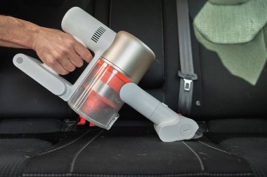 Siyah araba koltuğundaki kiri temizlemek için el yapımı elektrikli süpürge kullanan birinin yakın çekimi. İç döşeme temizleme aracı