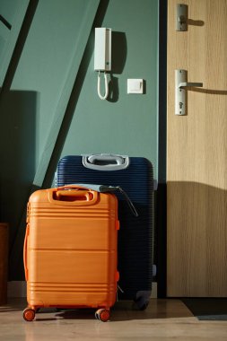 İki modern bavul, turuncu ve lacivert, sabah ışığında giriş kapısının yanında durun. Oturma odasındaki bavullar tatil için hazır. Seyahat hazırlığı kavramı