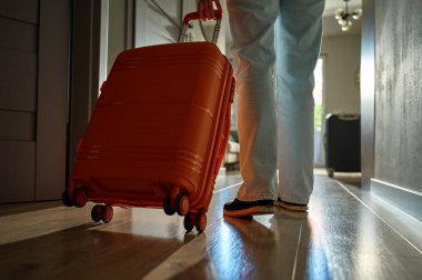 Dolaşan bavullarla kapıya doğru yürüyen bir gezginin arka görüntüsü. Koridorda turuncu bavulla yürüyen kişi. Ayrılma ve tatil için evden ayrılma kavramı