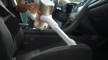 Adam araçta koltuk döşemesini temizlemek için el yapımı elektrikli süpürge kullanıyor. Modern araba temizliği ve bakımı