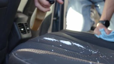 Kumaş araba koltuğuna köpük temizleyici sıkan ve iç temizlik sırasında bezle silen kişi. Araç döşemesi bakımı. Araba derin temizlik ve temizlik.
