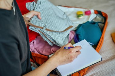 Seyahate hazırlanan bir kadın, bavulunu elbiseleriyle dolduran ve seyahat listelerini kontrol eden bir kadın. Tatil ve tatil planlama kavramı