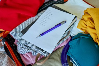 El yazısıyla kontrol listesi ve bavula doldurulmuş kıyafetlerin üzerindeki kalem. Yolculuğa hazırlanıyorum. Tatil ve tatil planlama