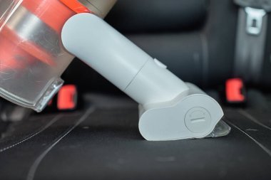 Kablosuz elektrikli süpürge, araba koltuğu döşemesini süpürüyor. Modern araba temizliği ve bakımı