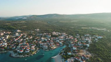 Geleneksel evleri, yeşil tepeleri ve turkuaz denizi olan küçük bir kasabanın havadan görünüşü. Adriyatik kıyı şeridi yakınlarındaki kıyı köyü. Hırvatistan 'ın Rogoznica kentinin manzarası