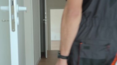 Tulumlu profesyonel bir tamirci koridorda elinde alet çantalarıyla yürüyor. İşçi işten sonra modern iç mekandan ayrılıyor. Ev onarımı veya yenileme kavramı