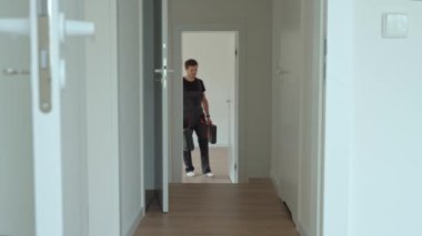 Tulumlu profesyonel bir tamirci koridorda elinde alet çantalarıyla yürüyor. Parlak modern iç mekanlara giren işçiler. Ev onarımı veya yenileme kavramı