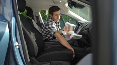 Adam kirli arabanın içini kablosuz elektrik süpürgesi kullanarak süpürüyor. Araba sahibi araçla, temizleme koltuğuyla ve iç döşemeyle ilgilenir. Rahat ve hijyen için günlük araç temizliği