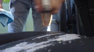 Kişi, oto koltuğuna temizlik köpüğü püskürtüp mikrofiber bez ile siler. İç temizlik sırasında. Araç döşemesi bakımı