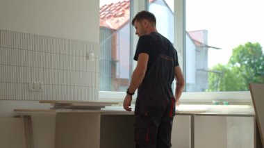 Tadilat sırasında mutfak mobilyalarını monte eden iş elbiseli bir adam. İşçiler yeni daireye mutfak dolapları kurmak için tahta panel kullanıyorlar. DIY ve marangozluk kavramı
