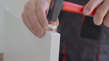 Çekiçle çiviyi yakın tut. İş kıyafetleri giymiş bir adam mobilya montajı için çekiç kullanıyor. DIY ev geliştirme konsepti