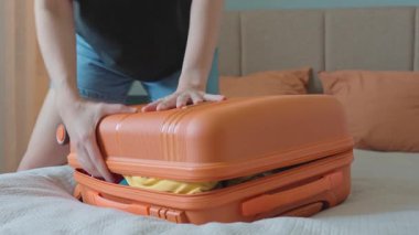 Kadın yatak odasına gitmek için giysilerini toplarken bavulu aşağı itiyor. Yolculuk için hazırlanan kadın