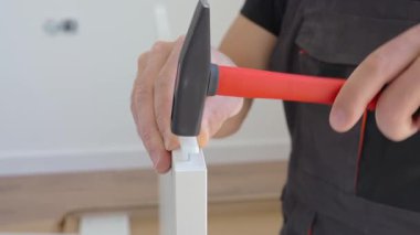 Çekiçle çiviyi yakın tut. İş kıyafetleri giymiş bir adam mobilya montajı için çekiç kullanıyor. DIY ev geliştirme konsepti