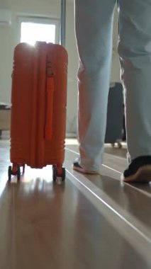 Dolaşan bavullarla kapıya doğru yürüyen bir gezginin arka görüntüsü. Koridorda turuncu bavulla yürüyen kişi. Ayrılma ve tatil için evden ayrılma kavramı