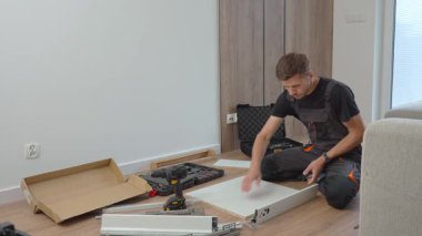 İş elbiseli bir adam oturma odasının zeminindeki aletleri kullanarak çekmeceleri birleştiriyor. DIY ev geliştirme ve mobilya kurulumu kavramı
