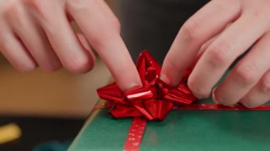 Noel hediyelerini paketleyen kadın, şen şakrak süveter giyiyor.