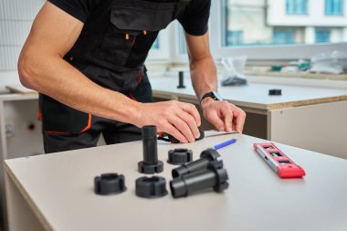 İnsan mutfak dolapları sırasında mobilya parçalarını ölçer, mezura, aletler ve plastik mobilya bacakları kullanır.