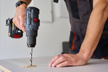Erkek eller elektrikli matkapla tahta deliyor. Marangozluk işi ev atölyesinde çalışıyor, yonga tahtasında delik açıyor.