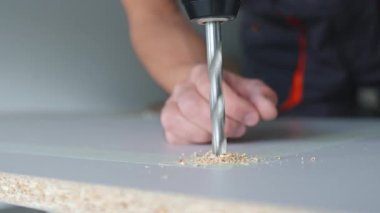 Erkek eller elektrikli matkapla tahta deliyor. Marangozluk işi ev atölyesinde çalışıyor, yonga tahtasında delik açıyor.