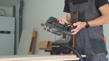 İş elbisesi işçisi ev atölyesindeki tezgahta elektrikli testereye elektrikli hortum bağlıyor. İş yerindeki adam odun kesmeden önce elektrikli yapbozu ayarlar. DIY projesi ve ev yenilemesi kavramı