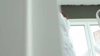 Koruyucu takım elbiseli, beyaz pantolonlu, siyah baskılı, yenileme sırasında tekerlekli paten kullanan bir kadın. İç duvarı boyayan kadın işçi. Evde tadilat ve iyileştirme kavramı