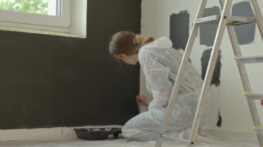 Ev tadilatı sırasında tek kullanımlık koruyucu takım elbiseli bir kadın duvarı fırçayla siyaha boyuyor. Cinsiyet eşitliği kavramı, kadın yetkinliği ve amelelik yapan kadınlar.