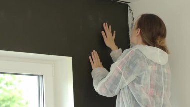 Koruyucu takım elbiseli kadın modern dairede yeni boyanmış koyu renkli duvarı inceliyor. DIY yenileme sırasında kalite denetimi kavramı