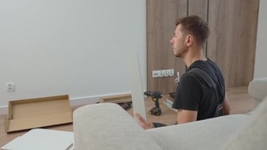 İş elbiseli bir adam oturma odasının zeminindeki aletleri kullanarak çekmeceleri birleştiriyor. DIY ev geliştirme ve mobilya kurulumu kavramı