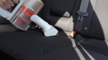 Siyah araba koltuğundaki kiri temizlemek için el yapımı elektrikli süpürge kullanan birinin yakın çekimi. İç döşeme temizleme aracı
