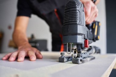İş elbisesi işçisi garajda tahta kesmek için kablosuz elektrikli yapboz kullanıyor. Atölyede çalışan yetenekli bir marangoz. Ev tadilatı yapan adam.