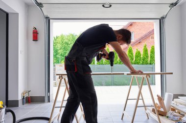 İş elbiseli bir adam, kablosuz matkap kullanarak tahta tahtada delik açıyor. DIY kavramı, kendi kendini tamir ve ev yenileme