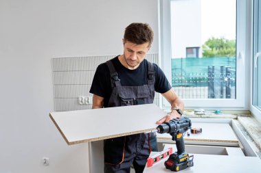 Üniformalı adam mutfak mobilyalarının kurulumu sırasında dolap panelini ölçüyor. Yeni dairede yenileme işlemi