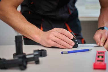 İnsan mutfak dolapları sırasında mobilya parçalarını ölçer, mezura, aletler ve plastik mobilya bacakları kullanır.