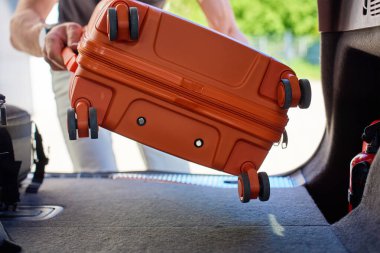 Turuncu bavulu evin dışında açık bir arabanın bagajına yükleyen adama yaklaş. Yolculuktan önce erkek yolcuların bagajlarını arabaya koyduğunu gördüm. Seyahat veya kalkıştan önce hazırlık