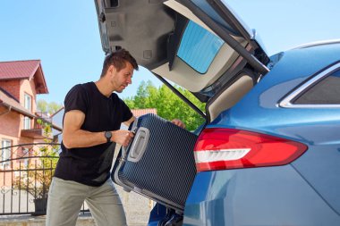 Güneşli bir günde bavulu bagaja yükleyen adam. Yaz seyahatine, tatile ya da bavulla yolculuğa hazırlanma kavramı