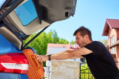 Banliyö evinin yanındaki bagajda turuncu bavulu iten adam. Bagajları araca yüklüyorum. Taşınma günü, taşınma ya da seyahat hazırlığı kavramı